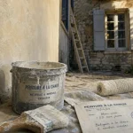 Peinture extérieur à la chaux sur mur enduit minéral, brosse et seau sur chantier